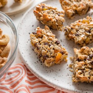 Close up of a homemade chocolate cashew apricot bar stacked on a white speckled ceramic plate.