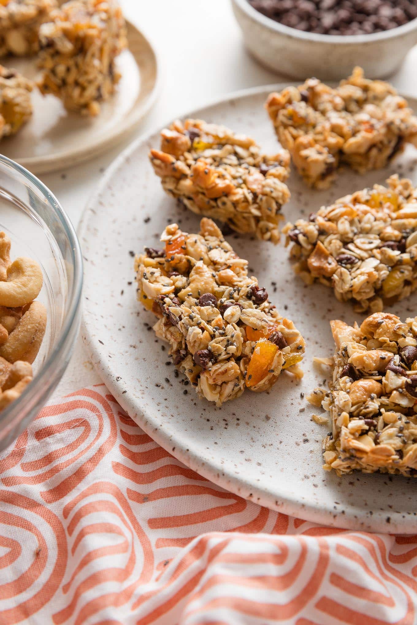 Close up of a homemade chocolate cashew apricot bar stacked on a white speckled ceramic plate.
