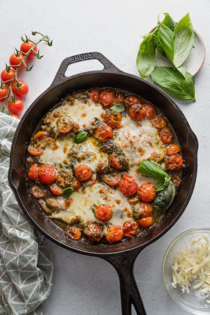 Cast iron skillet cooling on the counter full of a dish of chicken breasts baked with tomatoes, mozzarella, and pesto.