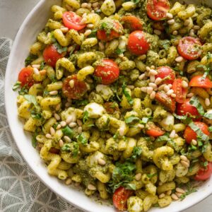 Large bowl filled with a pesto pasta salad with creamy mozzarella balls, juicy cherry tomatoes, and toasted pine nuts.