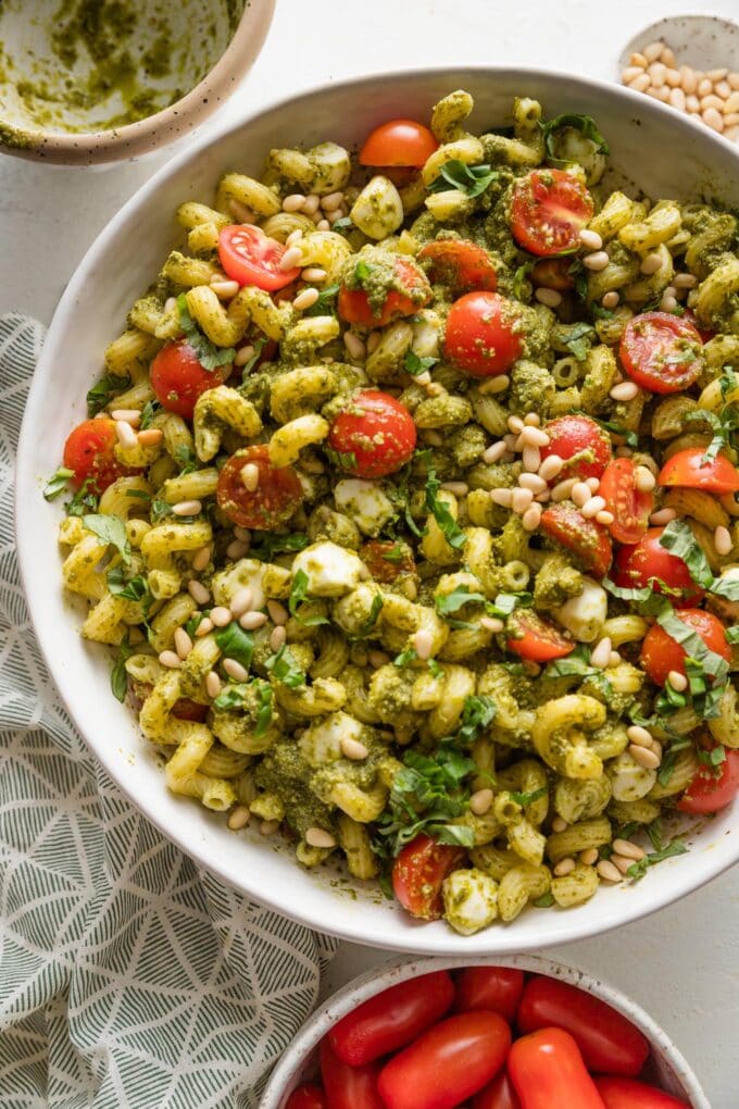 Large bowl filled with a pesto pasta salad with creamy mozzarella balls, juicy cherry tomatoes, and toasted pine nuts.