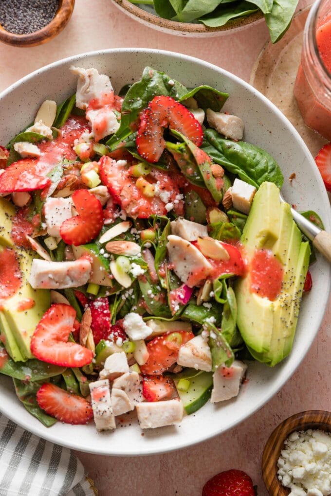 Close up of a salad with baby spinach, fresh strawberries, avocado, grilled chicken, red onion, and goat cheese.