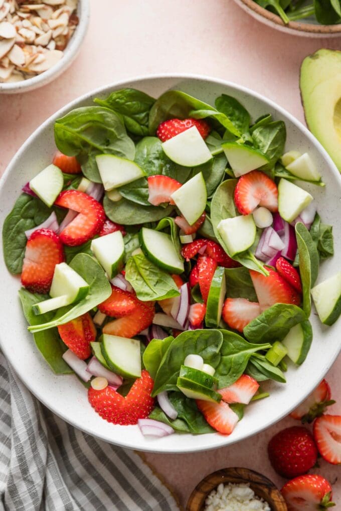 Bowl of baby spinach leaves, chopped cucumber, strawberries, and red and green onions.