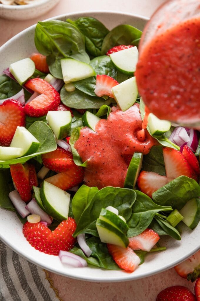Close up of homemade strawberry salad dressing being poured over a spinach strawberry salad.
