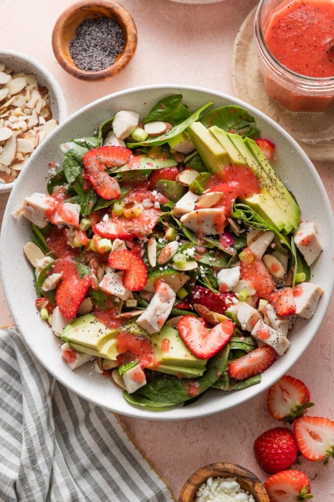 Bowl of strawberry spinach salad with chicken, almonds, goat cheese, and homemade strawberry salad dressing.