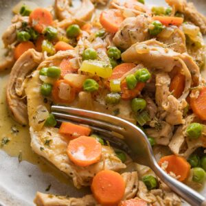 Close up of a fork pulling off a bite of creamy chicken and biscuits.