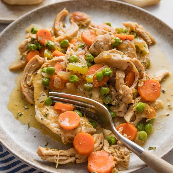 Close up of a plate full of creamy chicken and biscuits, with a fork pulling off a big bite.