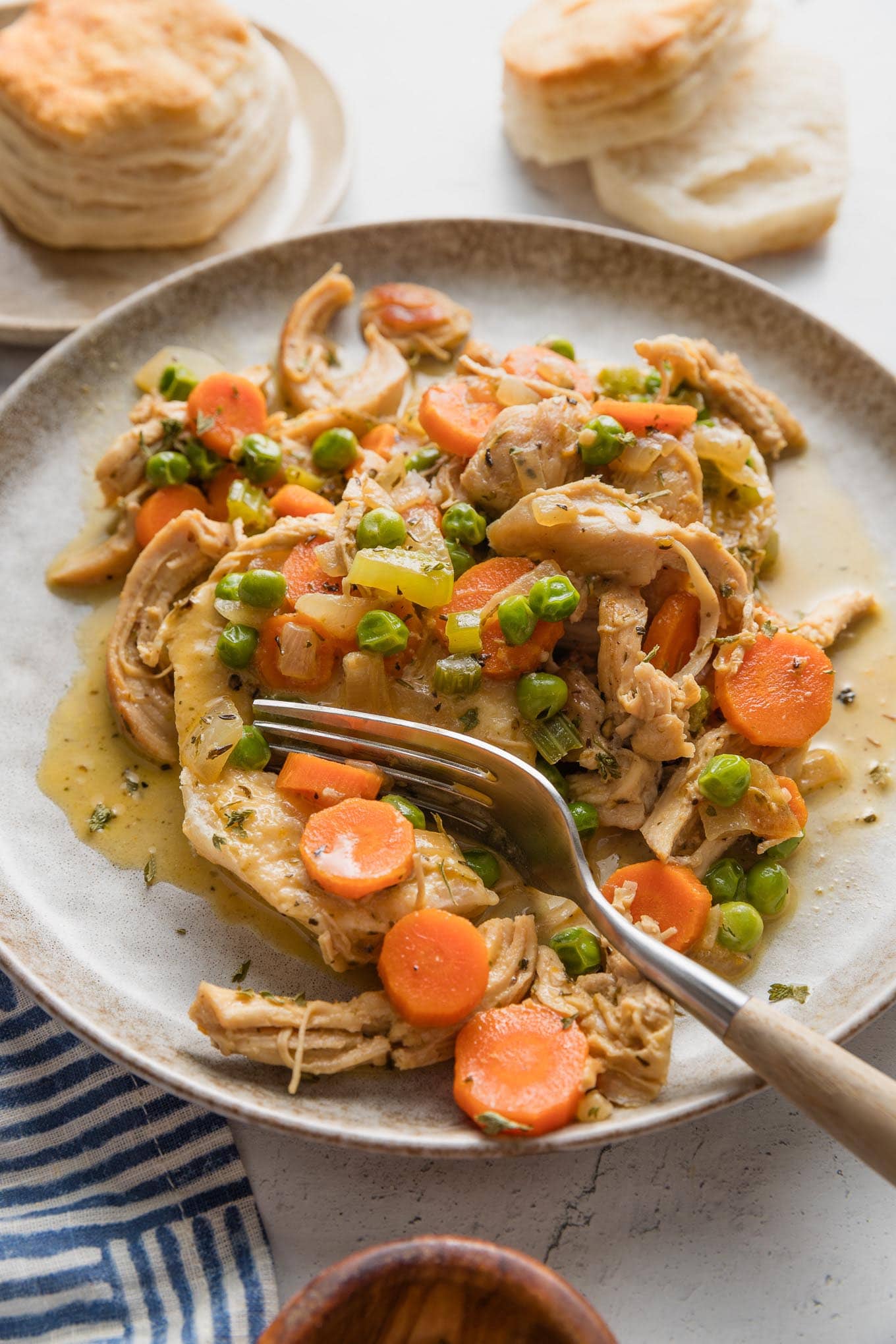 Close up of a plate full of creamy chicken and biscuits, with a fork pulling off a big bite.