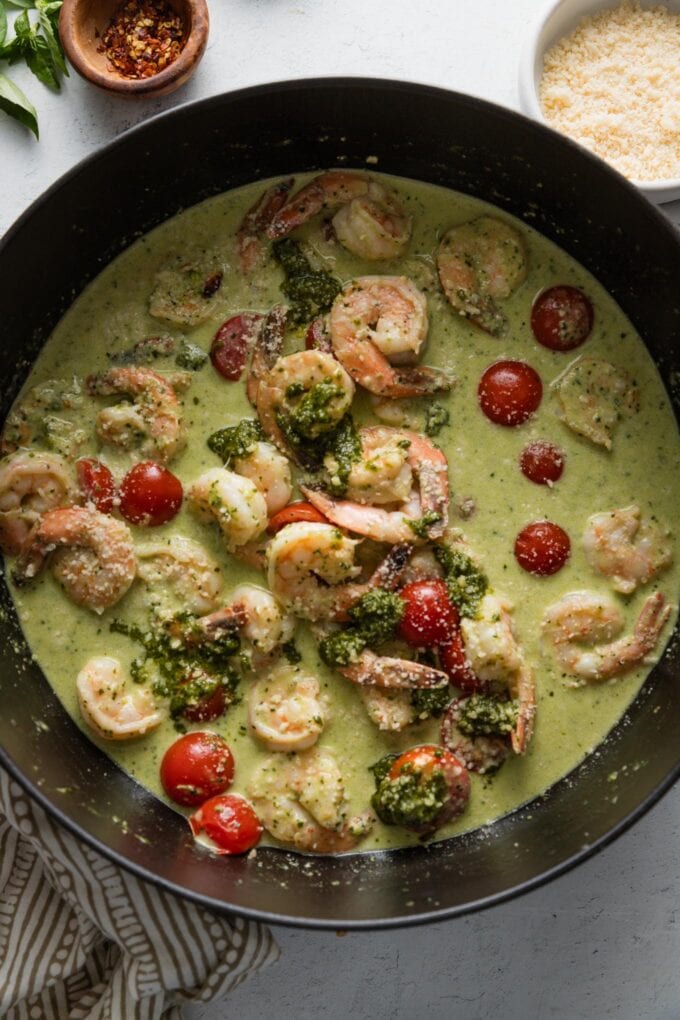 Deep cast iron skillet full of shrimp cooked with a homemade pesto cream sauce.
