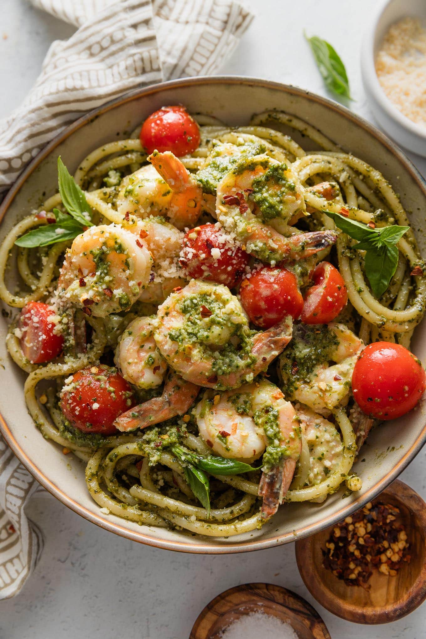 Bowl of creamy pesto shrimp with burst cherry tomatoes served over bucatini with extra grated Parm on top.