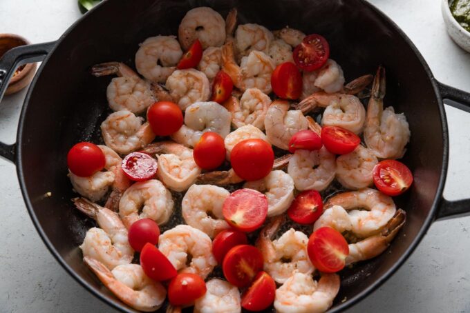 Shrimp cooked with halved cherry tomatoes in a deep cast iron skillet.