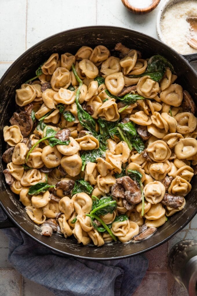Deep cast iron skillet full of a one pot creamy tortellini with mushrooms and spinach.