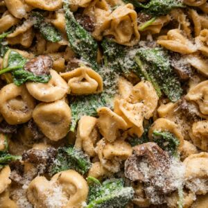 Close up of tortellini cooked in a pan with a quick homemade cream sauce, browned mushrooms, and wilted Parmesan.