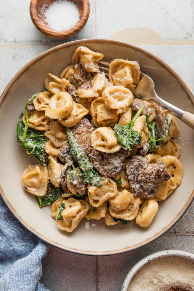 Bowl of creamy tortellini with baby spinach and browned mushrooms.