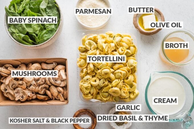Labeled overhead photo of fresh tortellini, sliced mushrooms, baby spinach, cream, broth, garlic, Parmesan, herbs, butter and olive oil.
