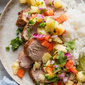 Plate with slices of grilled, seasoned pork tenderloin topped with a salsa of fresh pineapple, bell pepper, red onion, cilantro, and lime juice, served over white rice.