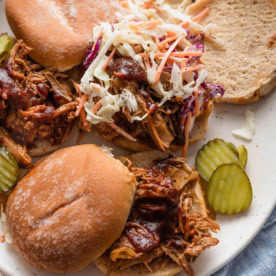 Platter filled with BBQ pulled pork sandwiches topped with homemade coleslaw and pickles.