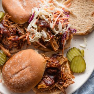 Platter filled with BBQ pulled pork sandwiches topped with homemade coleslaw and pickles.