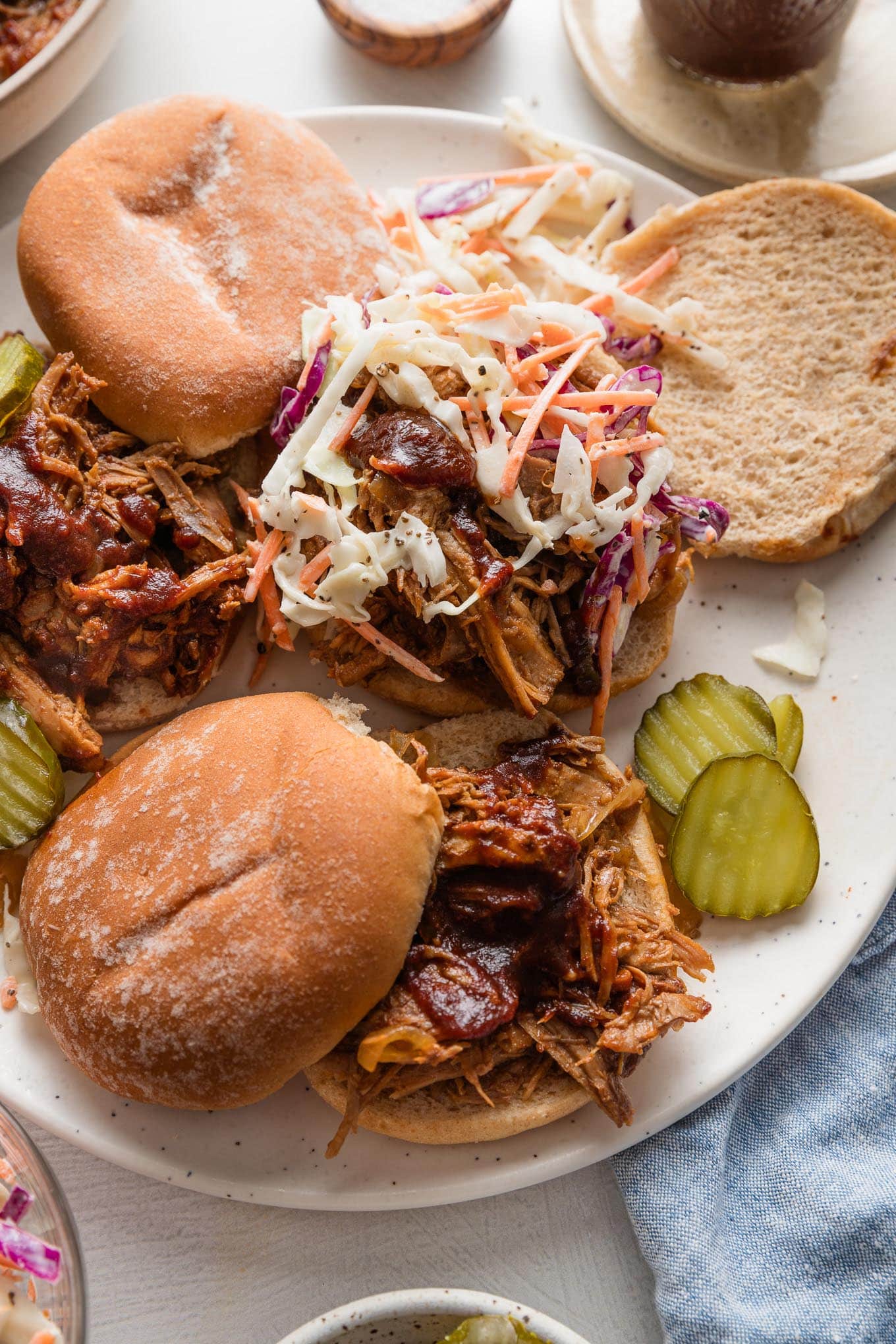 Platter filled with BBQ pulled pork sandwiches topped with homemade coleslaw and pickles.