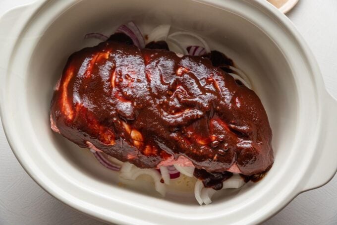 Pork shoulder in a Crockpot with garlic and BBQ sauce slathered on top.