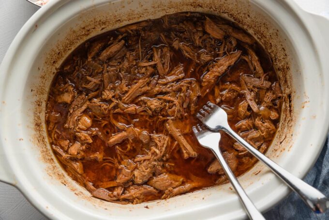 Two forks pulling apart pulled pork in a slow cooker.
