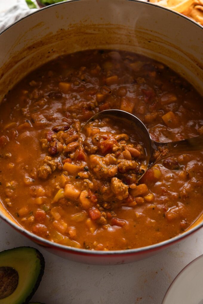 Close up of a ladle spooning up a helping of pumpkin chili made with lean ground turkey, diced tomatoes, bell pepper, and beans.