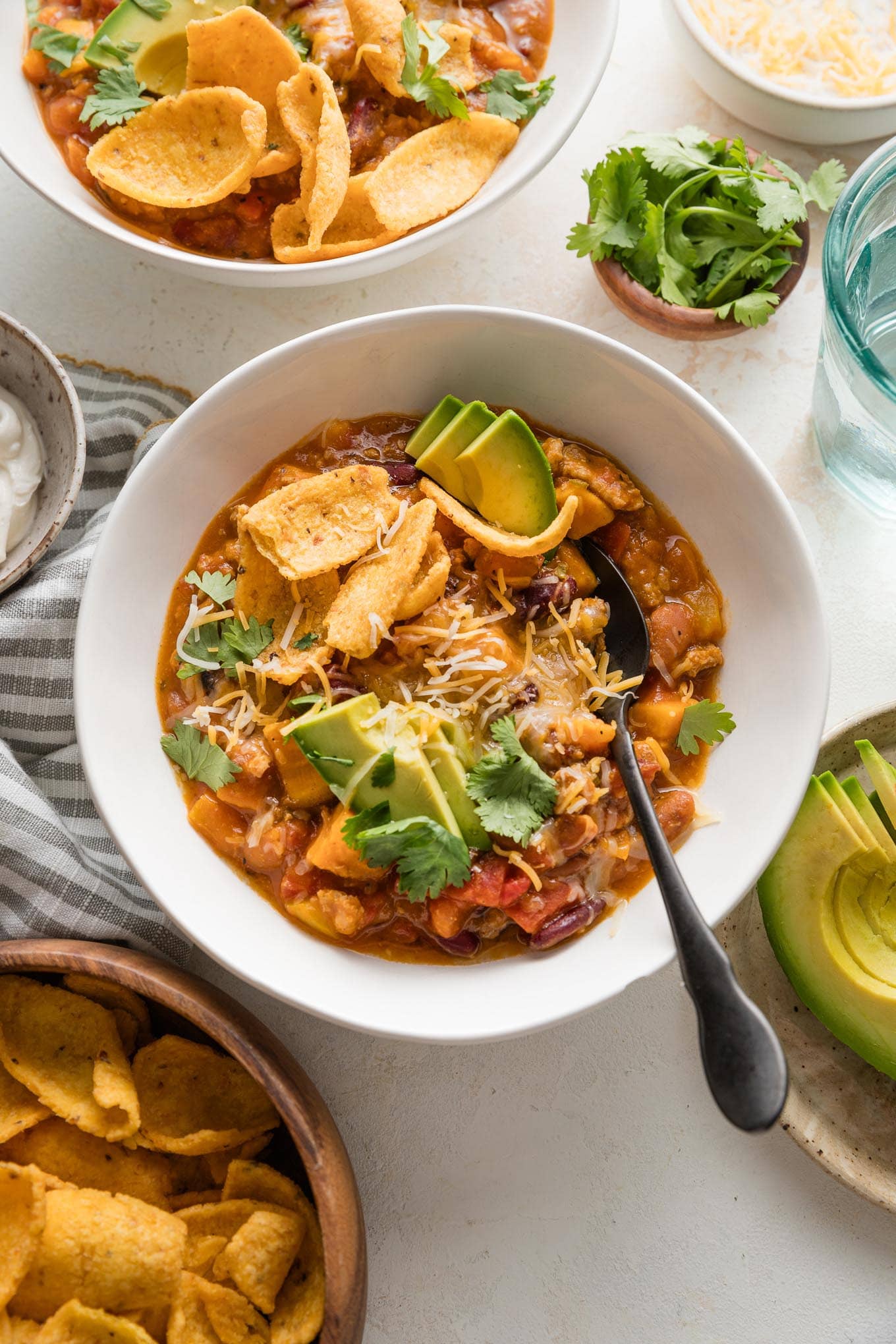 Bowl full of turkey pumpkin chili topped with fresh avocado, corn chips, cheese, and cilantro leaves.
