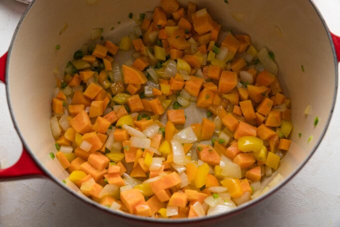 Diced sweet potato, onion, and bell pepper being sauteed in a very large Dutch oven.