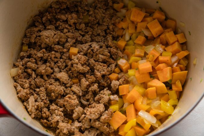 Browned and seasoned ground turkey cooked on one side of a very large red Dutch oven, with veggie medley softened on the other side.