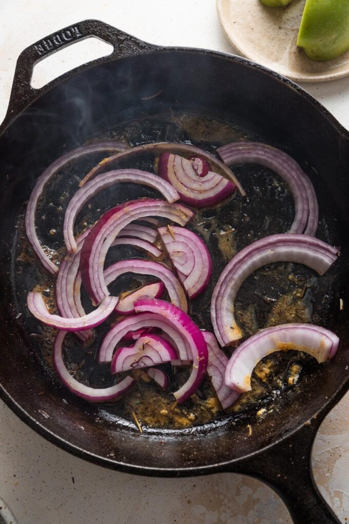 Red onion slices sizzling in a hot cast iron skillet.