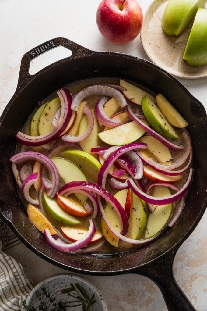 Apple cider and apple slices added to skillet with thinly sliced red onions.