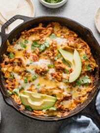 Overhead view of a chicken enchilada skillet with corn, green chiles, and toppings of fresh cilantro and sliced avocado.