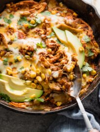 Spoon pulling a portion of enchilada skillet with chicken and corn out of a piping out cast iron pan.