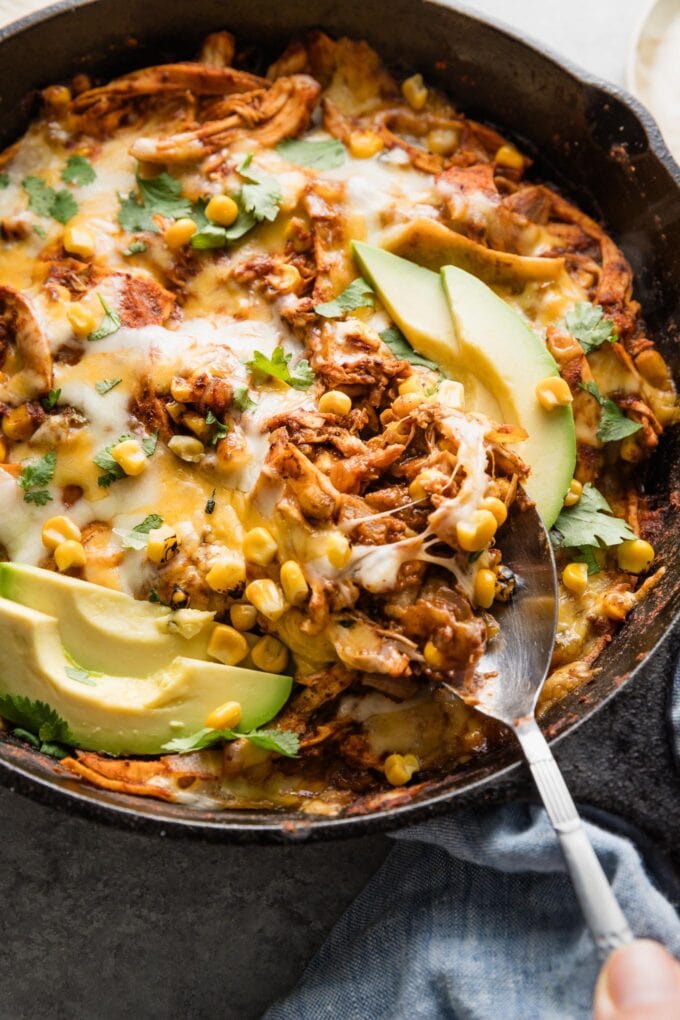 Spoon pulling a portion of enchilada skillet with chicken and corn out of a piping out cast iron pan.