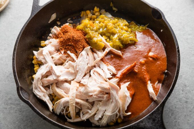 Chicken, sauce, taco seasoning, and chiles added to onion and corn in a skillet.