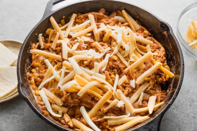Cheese sprinkled over a chicken enchilada skillet, ready to bake.