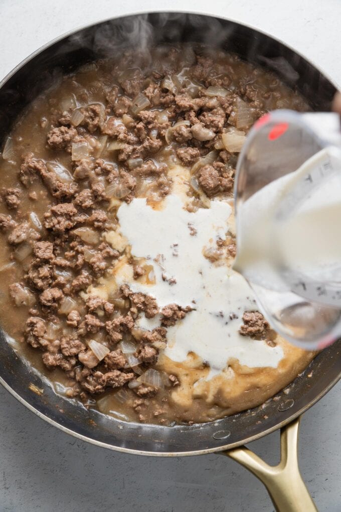 Cream being poured into gravy-like meat sauce.