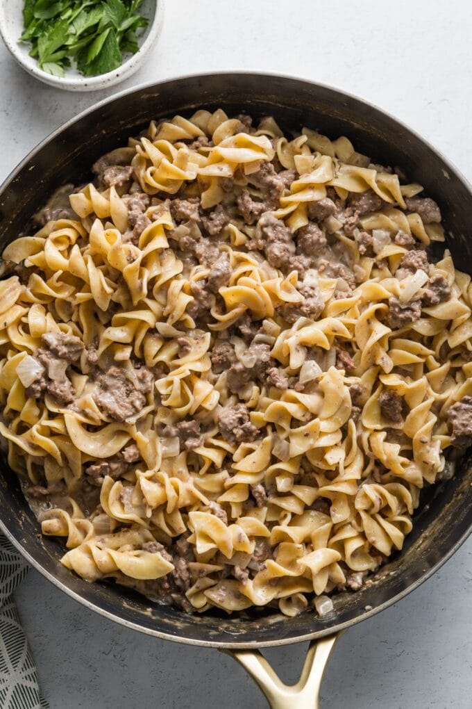 Overhead view of a large skillet with egg noodles and ground beef in sauce all mixed together.