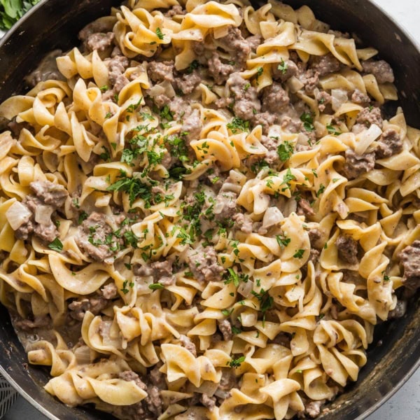 Skillet full of ground beef and noodles topped with fresh chopped Italian parsley.