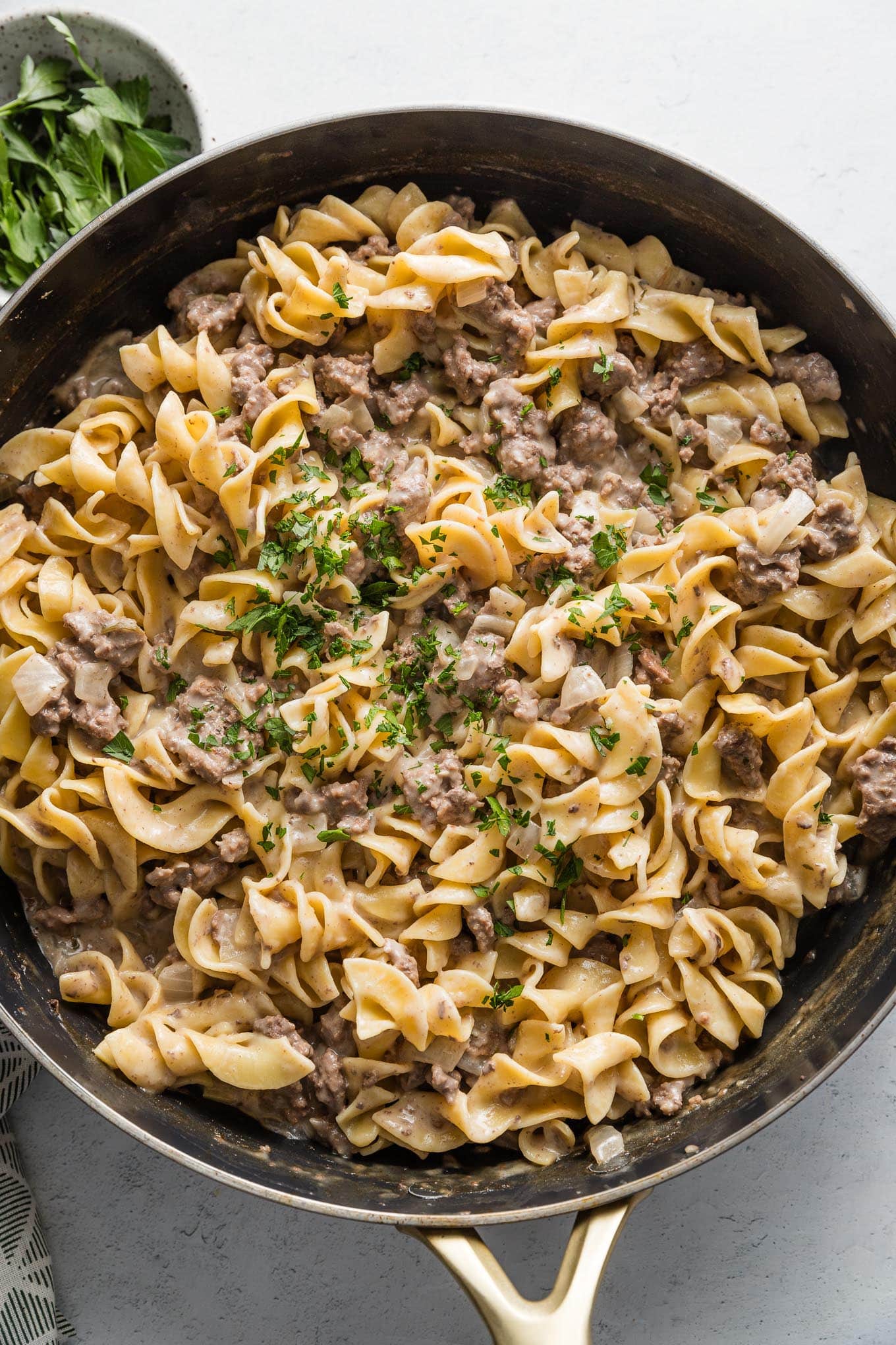 Skillet full of ground beef and noodles topped with fresh chopped Italian parsley.