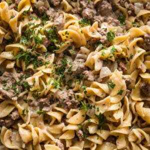 Close up of ground beef and noodles sprinkled with fresh chopped Italian parsley.