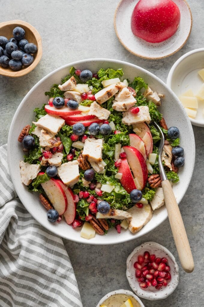 Forkful of kale apple salad with chicken and berries in a light lemon olive oil dressing.