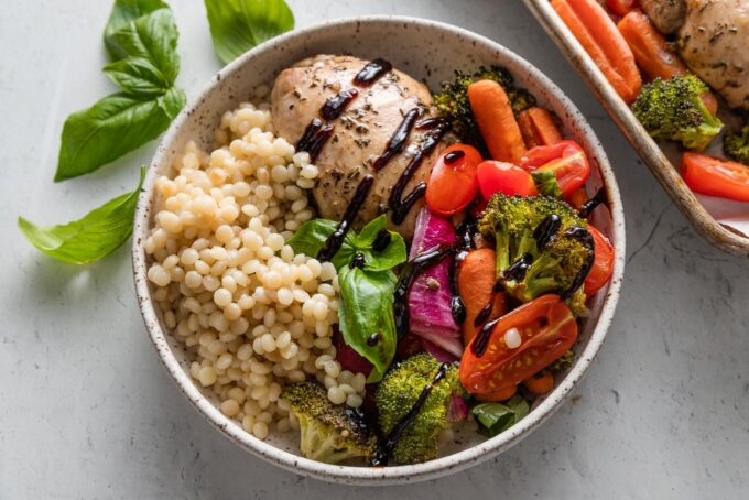 Sheet pan balsamic chicken and veggie bowl with pearl couscous and fresh basil.