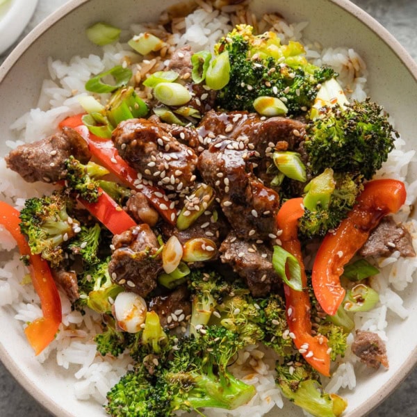Bowl of marinated sirloin tips served with roasted broccoli and red bell peppers.