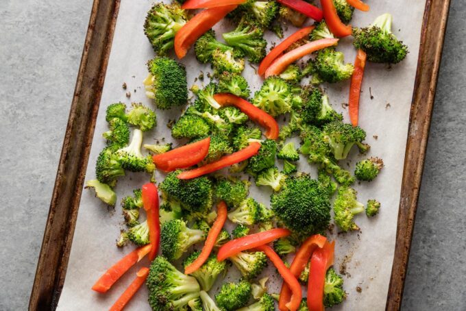 Broccoli and thinly-sliced red pepper together on a parchment-lined sheet pan.