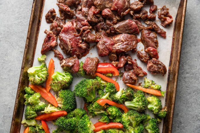 Marinated steak tips added to one side of a sheet pan to roast with bell pepper and broccoli florets.