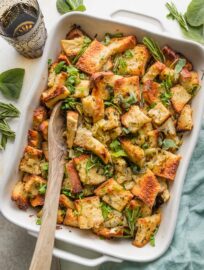Wooden serving spoon lifting up a helping of bread stuffing from a large pan.