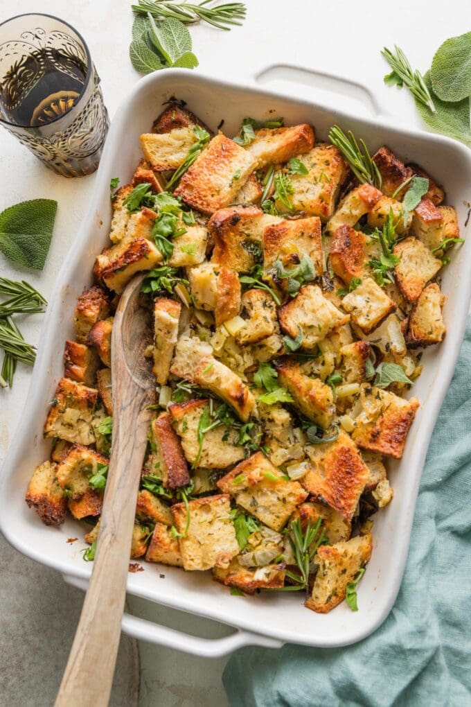 Wooden serving spoon lifting up a helping of bread stuffing from a large pan.
