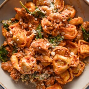 Bowl filled with tortellini and Italian sausage with baby spinach in a homemade tomato cream sauce, topped with freshly grated Parmesan cheese.