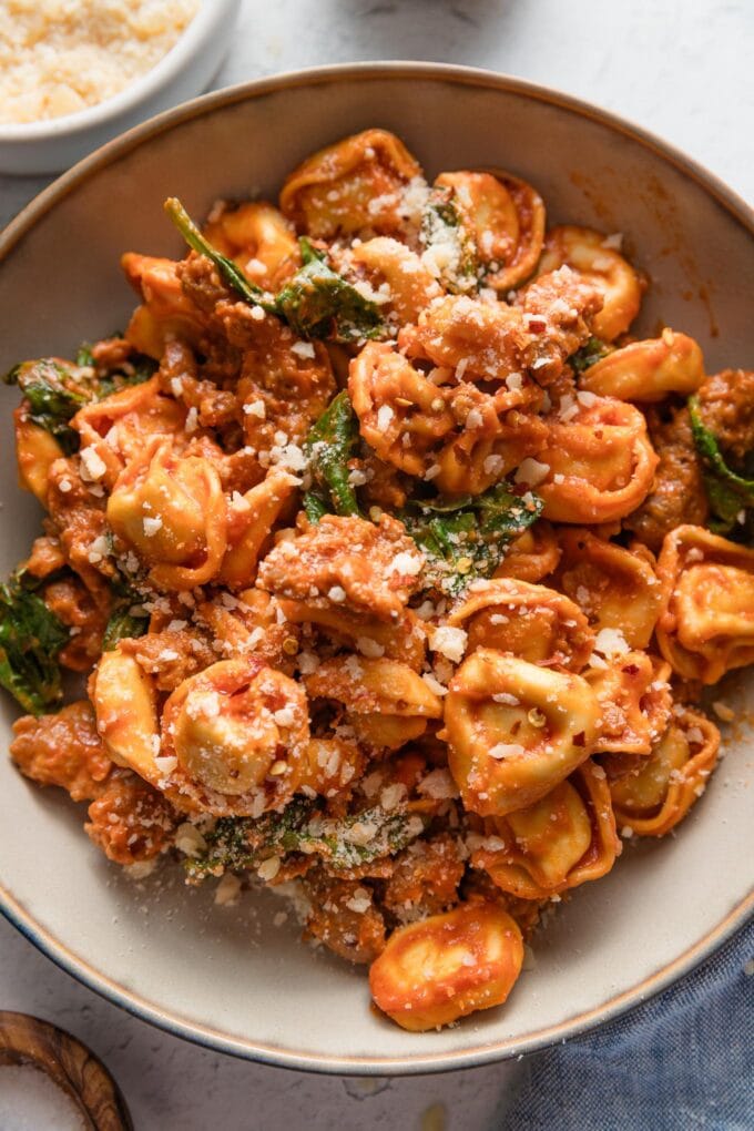 Bowl filled with tortellini and Italian sausage with baby spinach in a homemade tomato cream sauce, topped with freshly grated Parmesan cheese.
